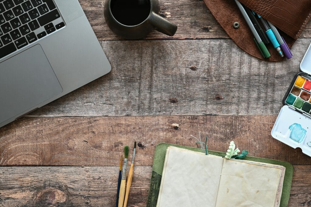 A freelancer working at a kitchen table with a laptop, calculator, and receipts spread out